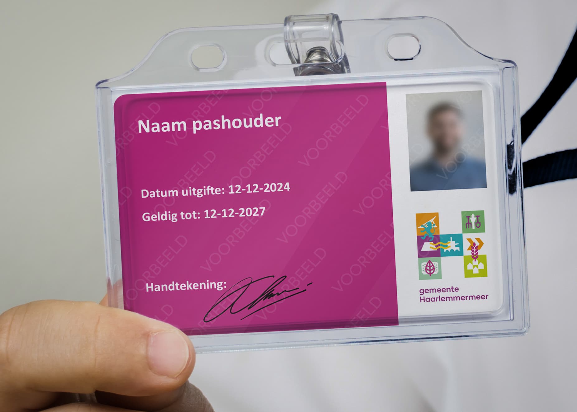 Voorbeeld van een GIK-pas met roze achtergrond. Links staan velden voor naam, datum van uitgifte (12-12-2024), geldigheid (12-12-2027) en een handtekening. Daaronder staat de handtekening van de pashouder. Rechtsboven is een pasfoto zichtbaar. Rechtsonder staan het logo van de gemeente met meerdere gekleurde iconen met daaronder de tekst 'gemeente Haarlemmermeer'. De pas zit in een doorzichtige plastic houder met een bevestigingsclip.