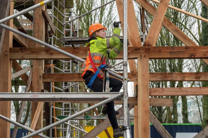 bouwvakker op steiger bij houten geraamte van de hoeve