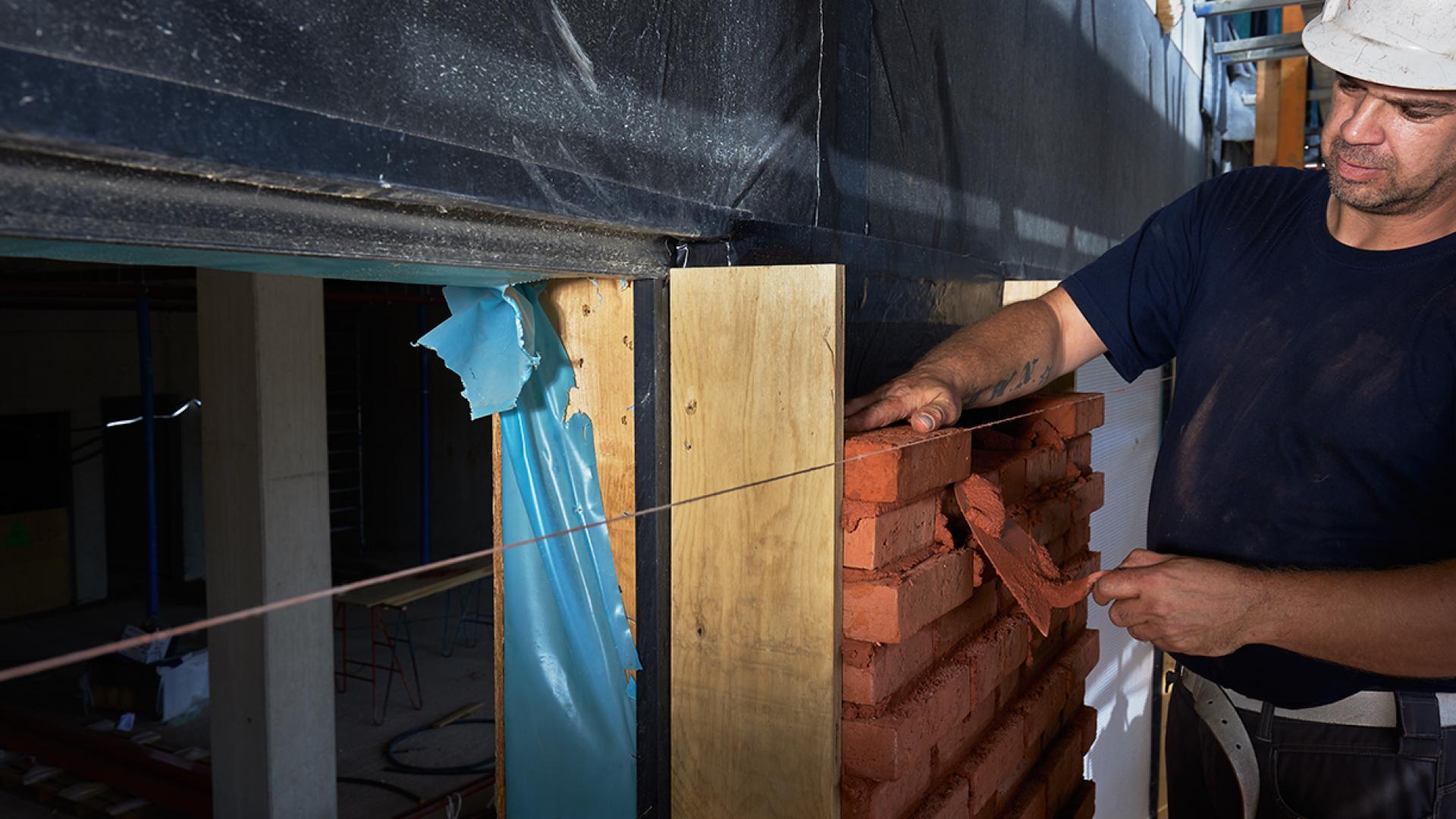 Een metselaar bouwt aan een nieuwe woning. Hij metselt de muur.