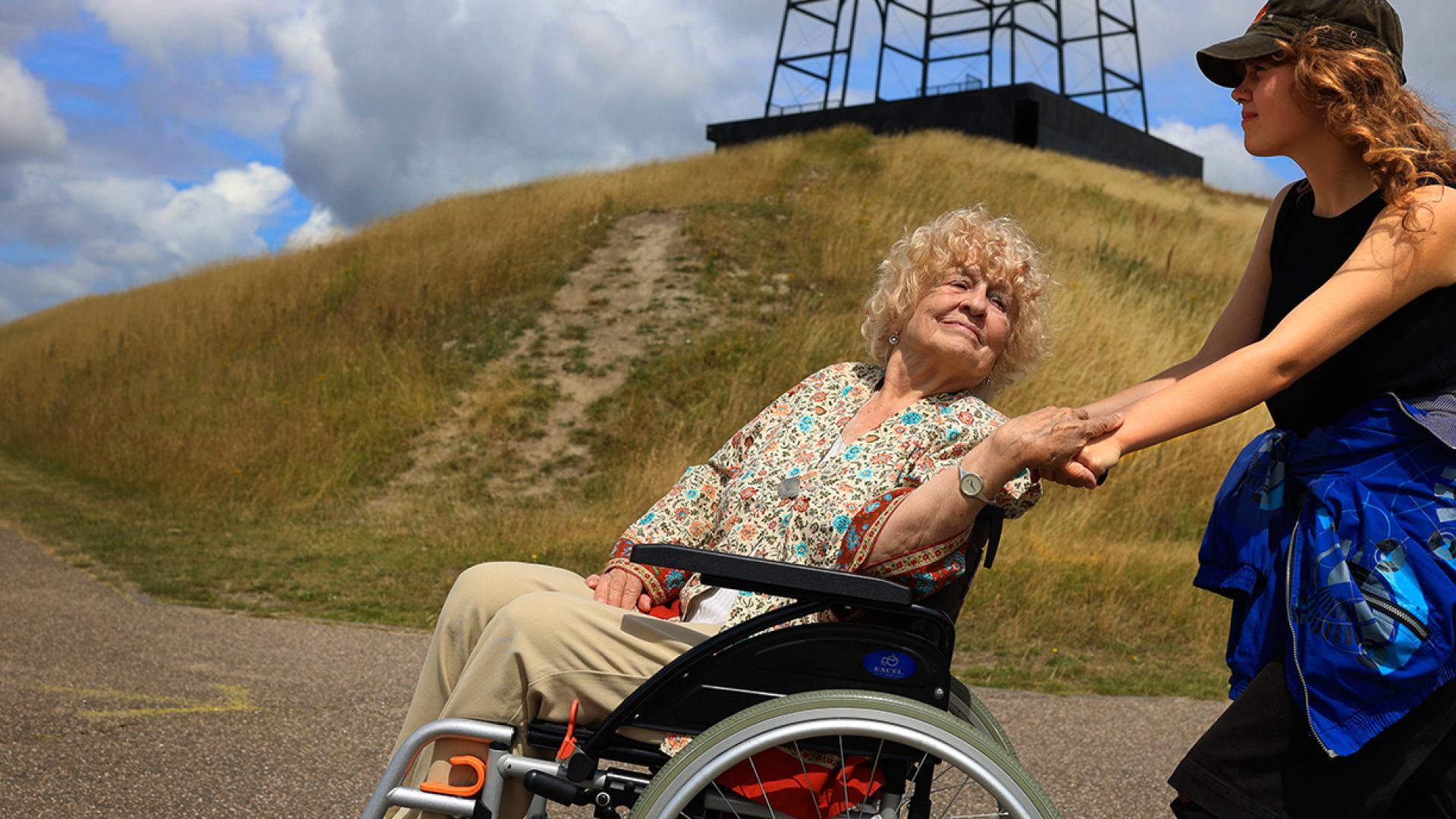 Een kleindochter duwt haar oma in een rolstoel. Ze wandelen samen bij de Big Spotters Hill in Hoofddorp.