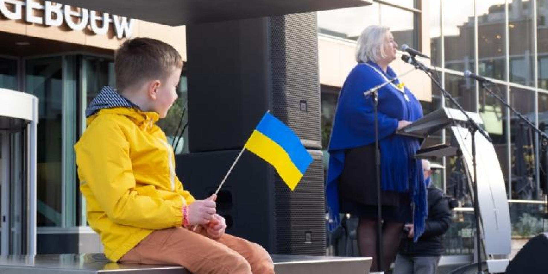 Jongetje met Oekraïense vlag kijkt naar burgemeester Marianne Schuurmans die een toespraak houdt voor het Cultuurgebouw
