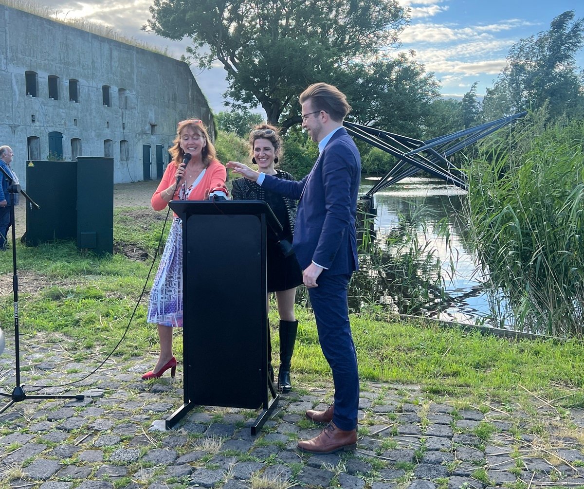 Wethouder Marja Ruigrok, kunstenares Siba Sahabi en architect Serge Schoemaker slaan gezamenlijk op een grote knop. Op de achtergrond het kunstwerk.n gezamenlijk op de grknop