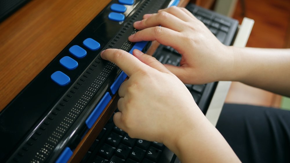 Twee handen lezen een brailleregel