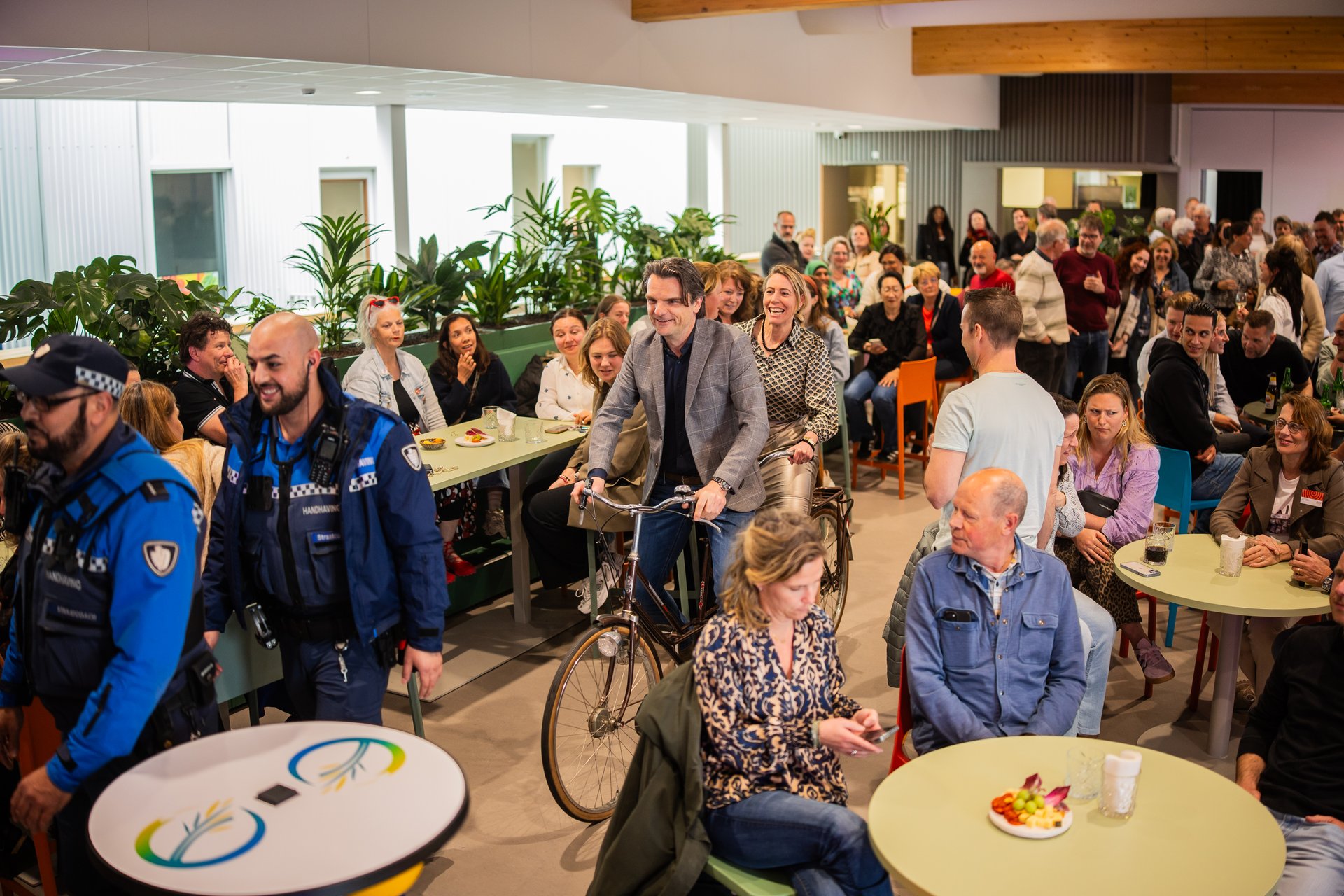 Directeuren Nienke Spanjerberg en Eric van de Reep rijden samen op een tandem de aula binnen. 