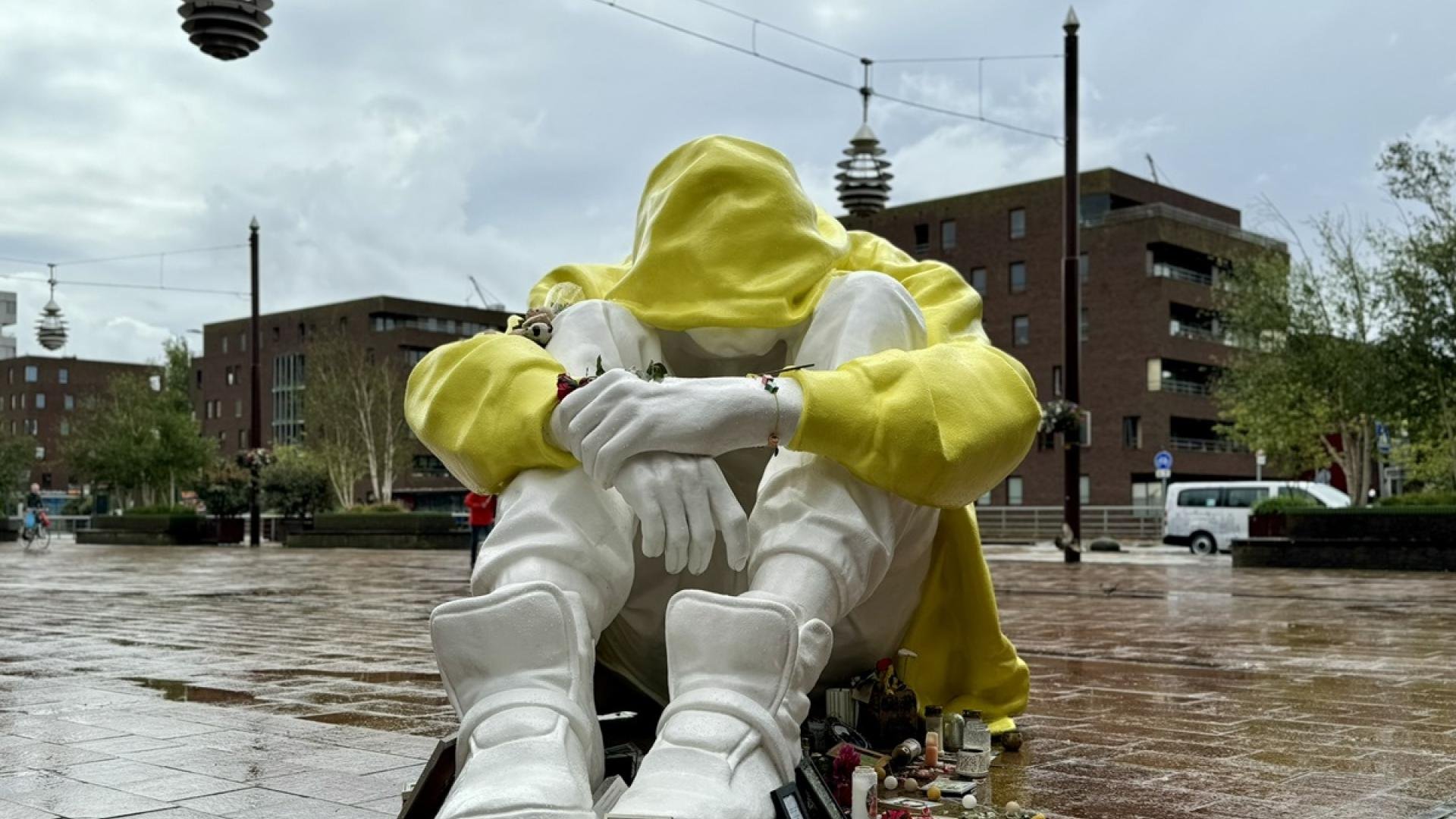 Meer dan levensgroot beeld van een jongere die ineengedoken zit met armen over de knieën. Beeld is uitgevoerd met wit materiaal, alleen de hoodie is geel.