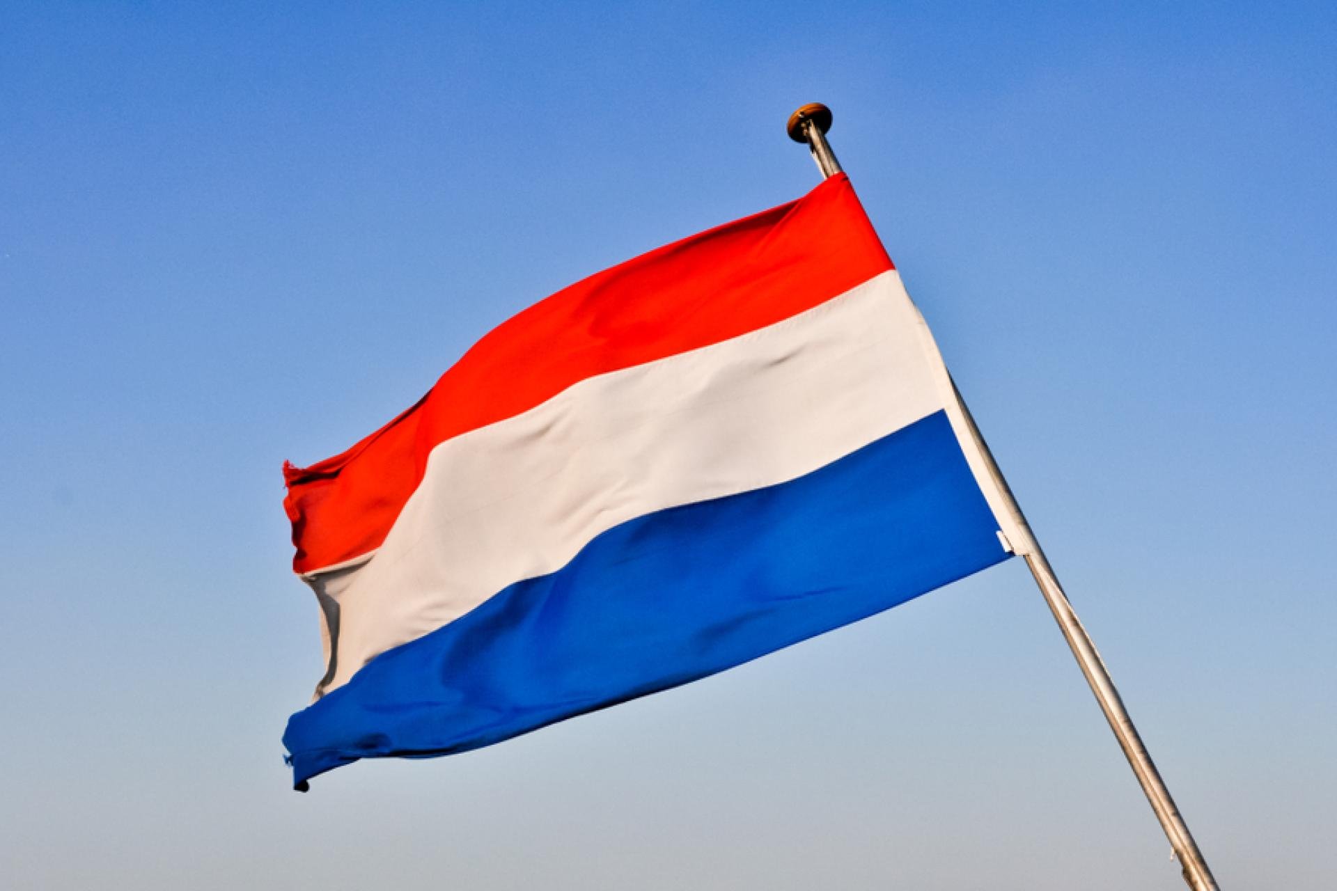 De Nederlandse vlag met op de achtergrond een blauwe lucht